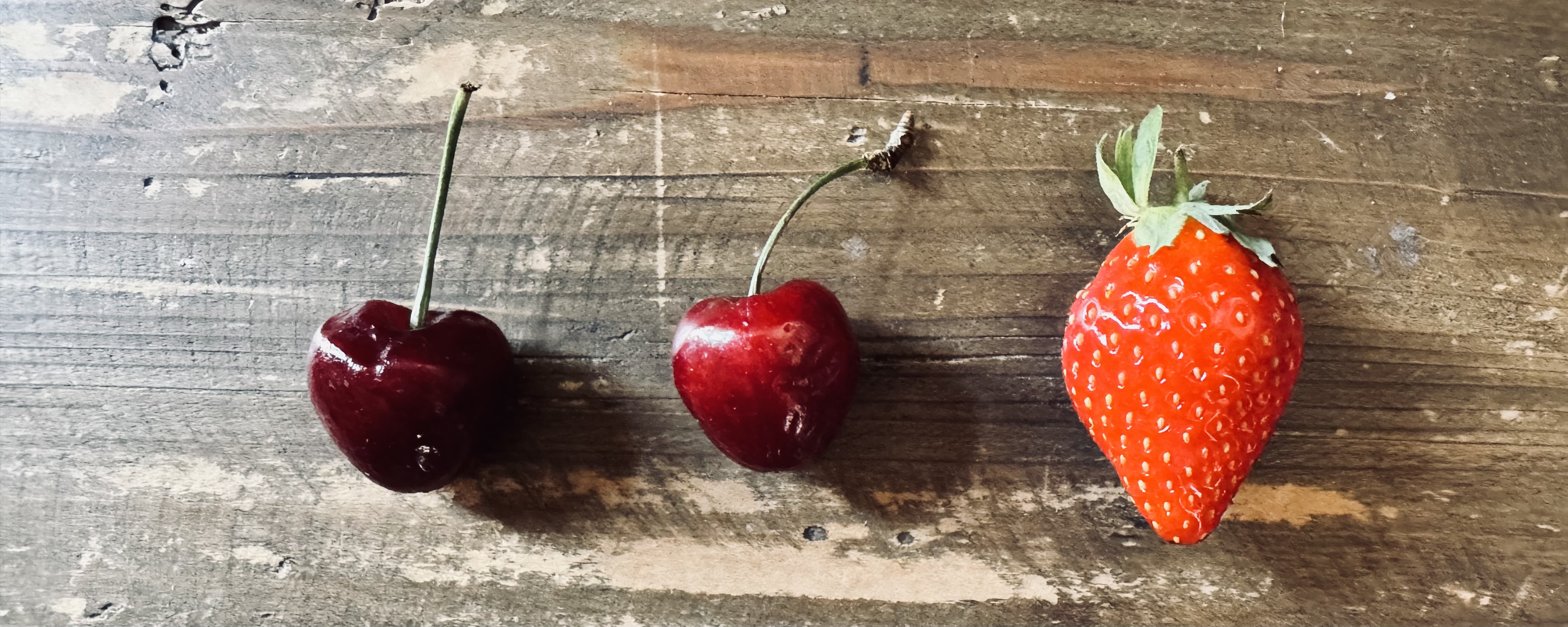 A photo of two cherries and a strawberry on a wooden counter